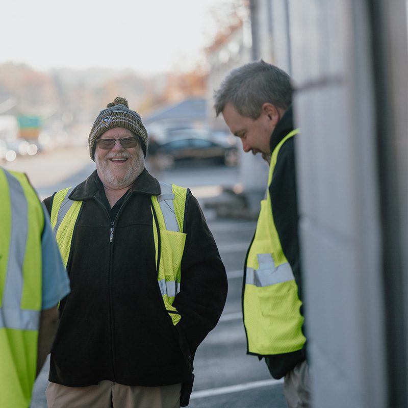 A smiling man wearing a winter beanie, glasses, and a safety vest standing outdoors alongside other parking team volunteers at Freedom Church in Murrysville, PA.